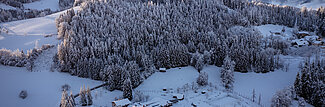 Verschneites Hotelresort am Waldrand mit Alpenpanorama bei Sonnenaufgang