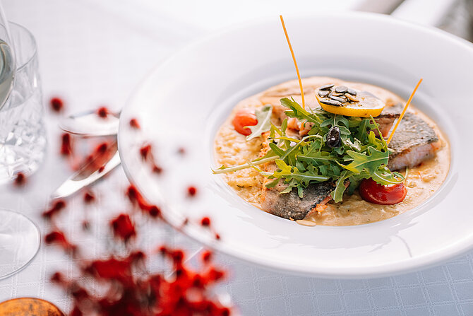 Gourmetgericht mit gegrilltem Fisch, Risotto, Rucola und Kirschtomaten auf weißem Teller